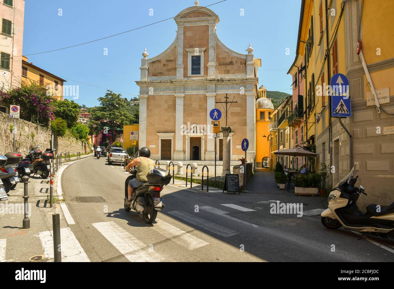 A man on a scooter passing on the road in front of the church of Saint Francis in the old sea town, Lerici, La Spezia, Liguria, Italy Stock Photo