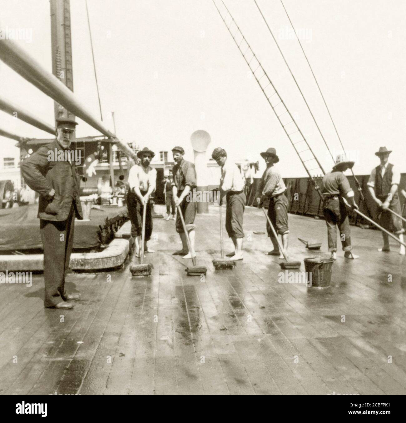 Sailors swabbing down and cleaning the decks of the ship 'Bancoora' whilst moored in Sydney Harbour, NSW, Australia c. 1910 The 'Bancoora' was built in Glasgow in 1880. It weighed 2880 tons. She was was stranded near Torquay, Victoria, Australia in 1893 but was re-floated. This image is from a very small and retouched print in an old Australian photograph album. Stock Photo