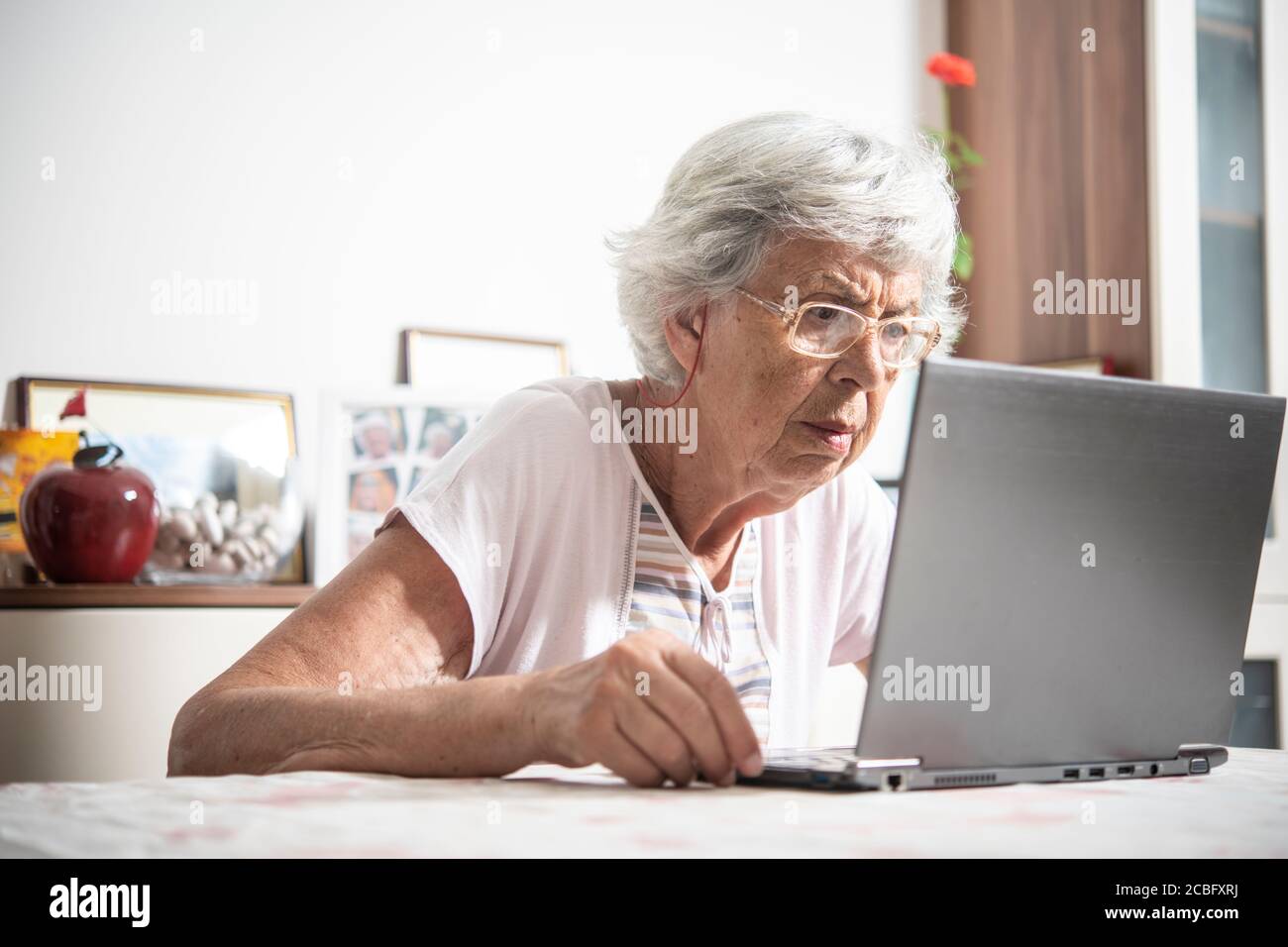 An elder lady with glasses staring at laptop's monitor while clicking ...