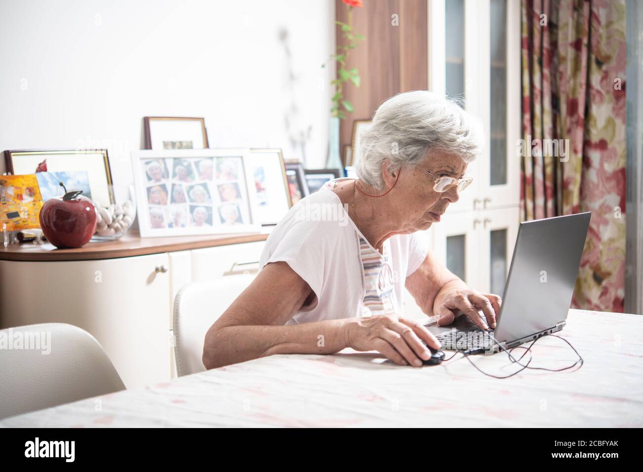 An elder lady with glasses staring at laptop's monitor while clicking ...
