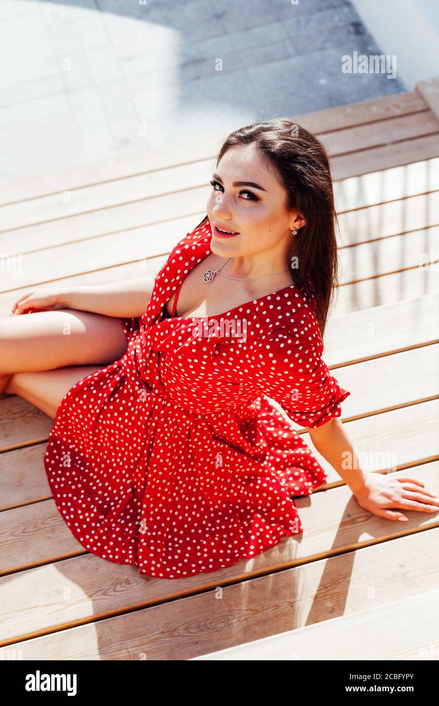 Beautiful fashionable brunette woman in summer red dress sits on the steps  Stock Photo - Alamy