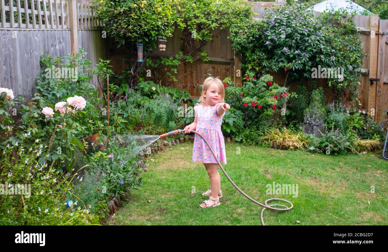 Young 3 year old girl watering a small city garden with a hose UK Stock Photo