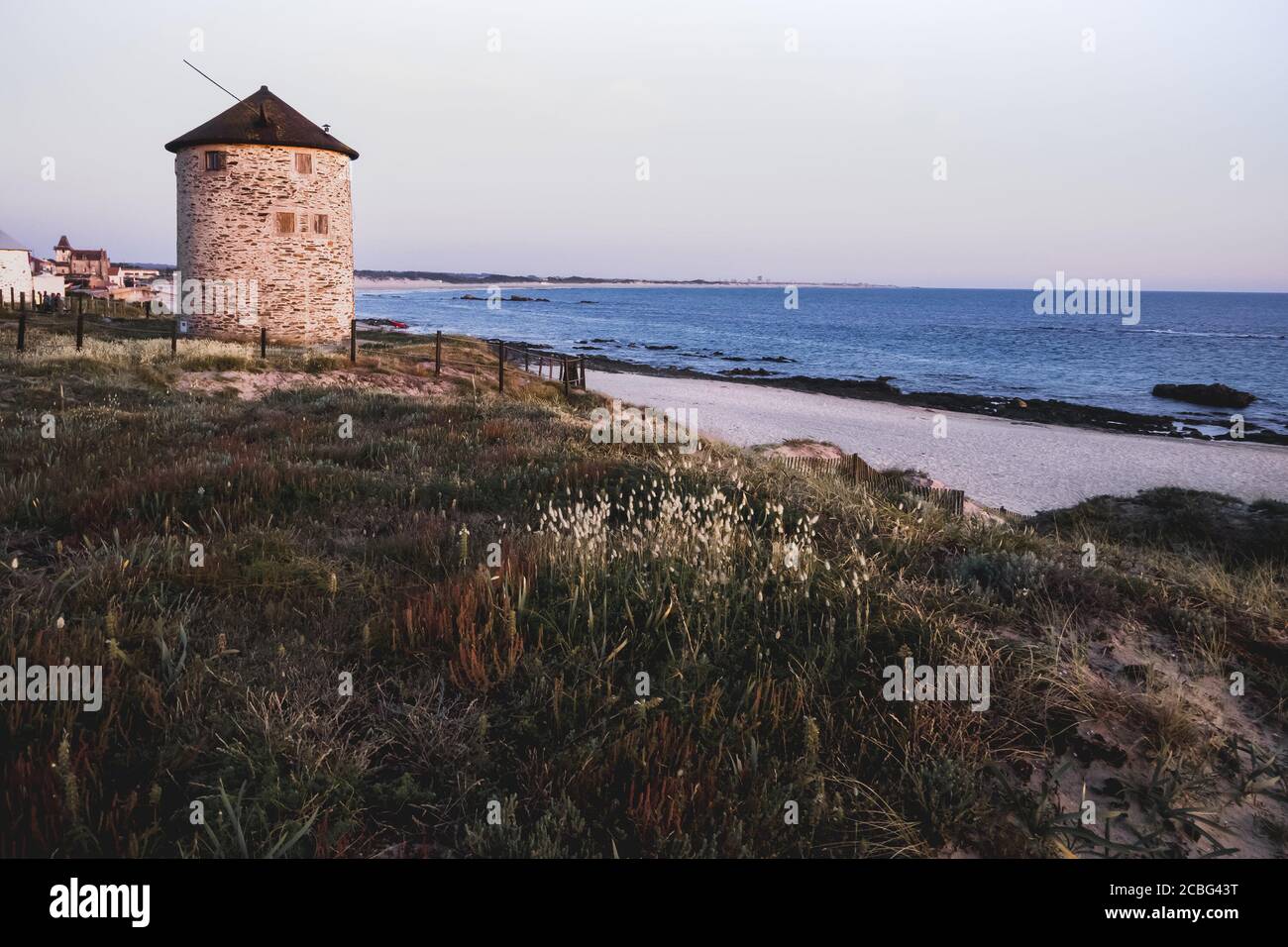 Stone windmill on Apulia beach, Portugal. View of the atlantic ocean from a grassy dune. Stock Photo