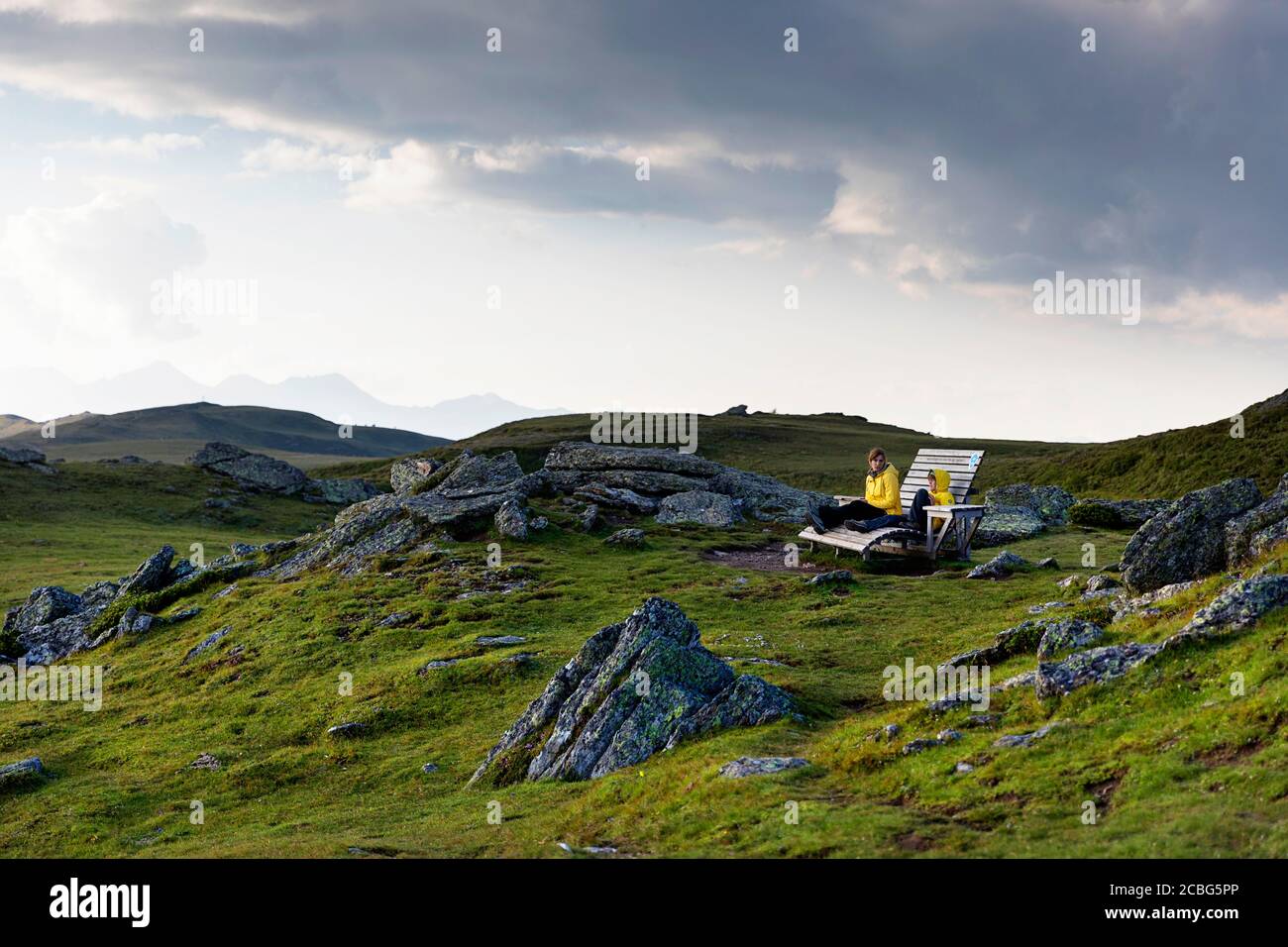 Mother and son sitting on wooden bench, having a good time outdoors on mountain with a view over the lake, Granattor, Lammersdorf Mountain, Austria Stock Photo