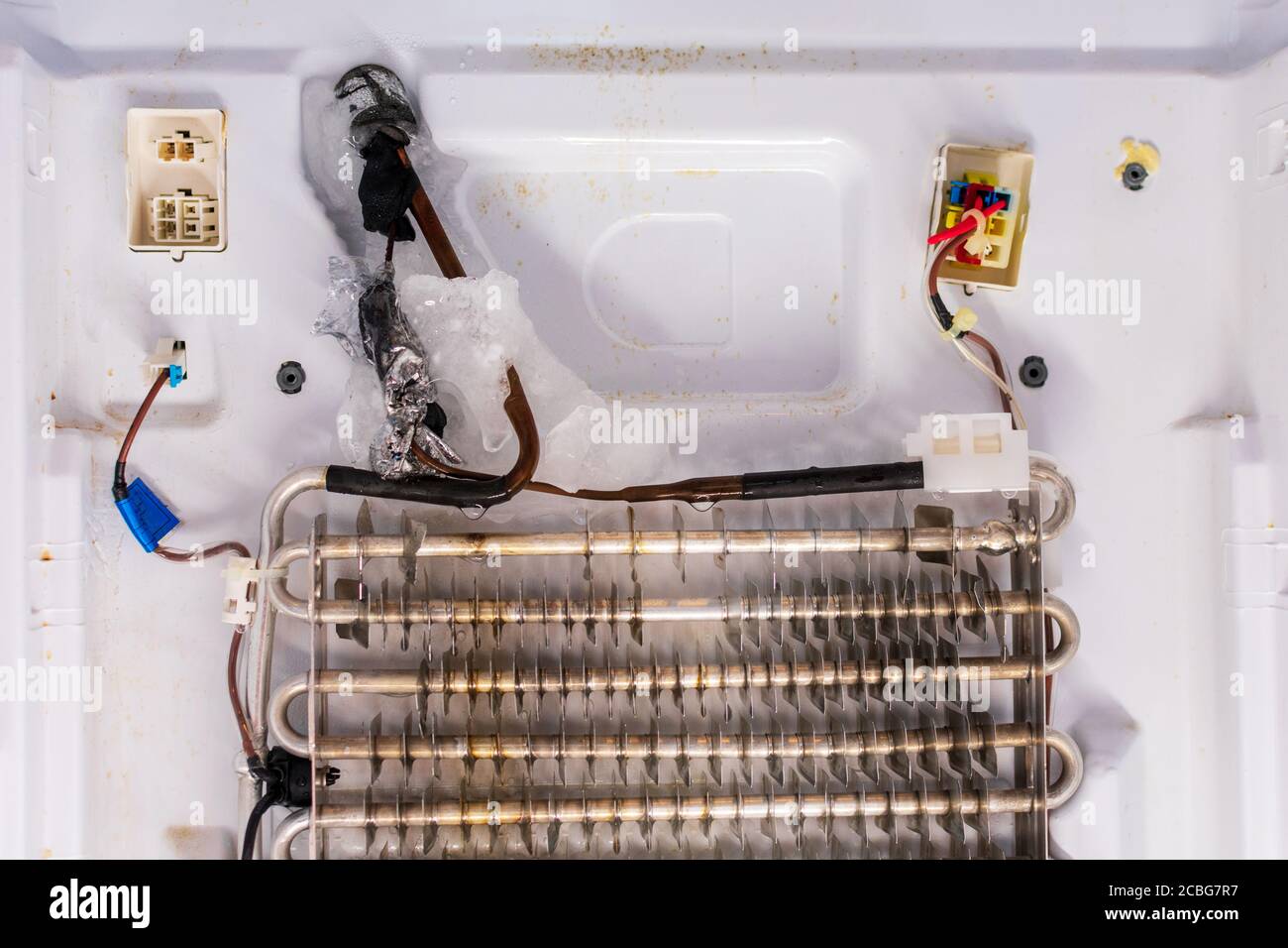 Refrigerator repair. Freezer compartment back panel removed. Evaporator coils with a frozen thermostat. Stock Photo