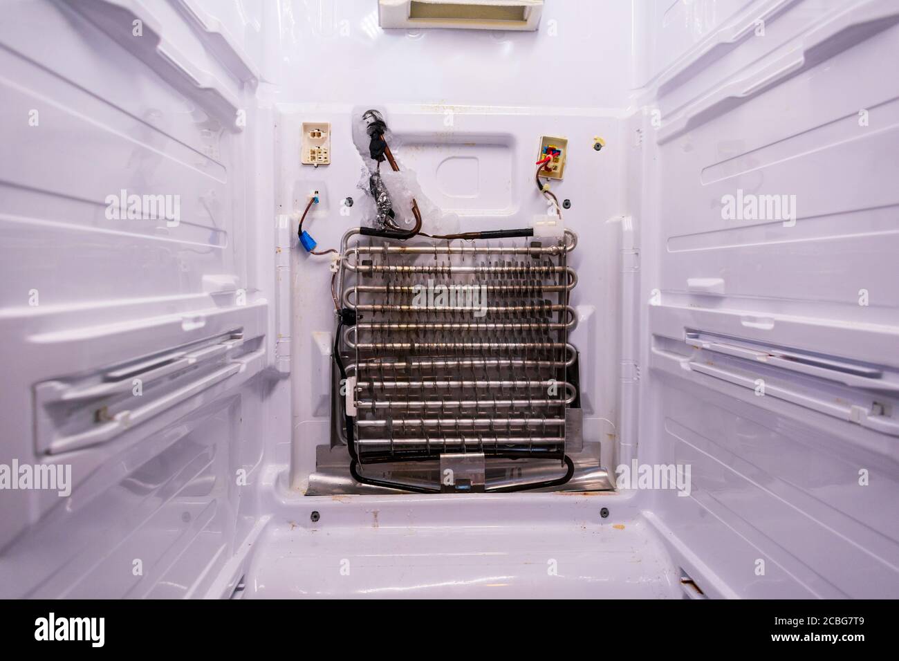 Refrigerator repair. Freezer compartment back panel removed. Evaporator coils with a frozen thermostat. Stock Photo