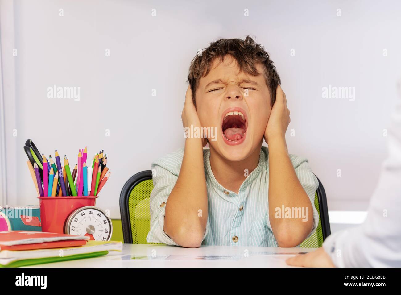 Autistic boy scream and close ears in pain during ABA development therapy sitting by the table in class Stock Photo