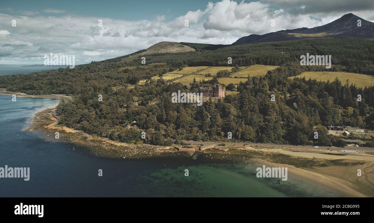 Scotland's Arran island landscape aerial zooming view: forests, meadows, mountains at summer day. Clouds on skyline near Goat Fell peak. Epic scene of Stock Photo