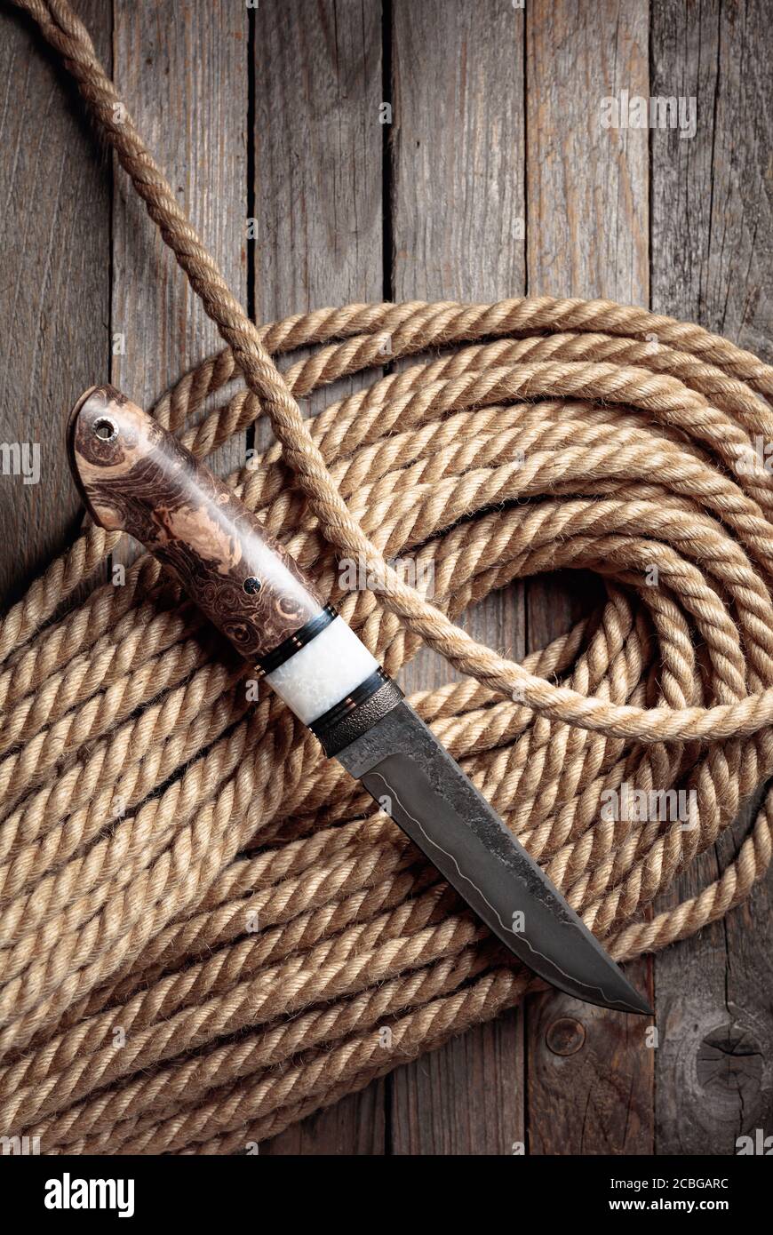 Hunter knife and hemp rope on wooden background. The surface of the