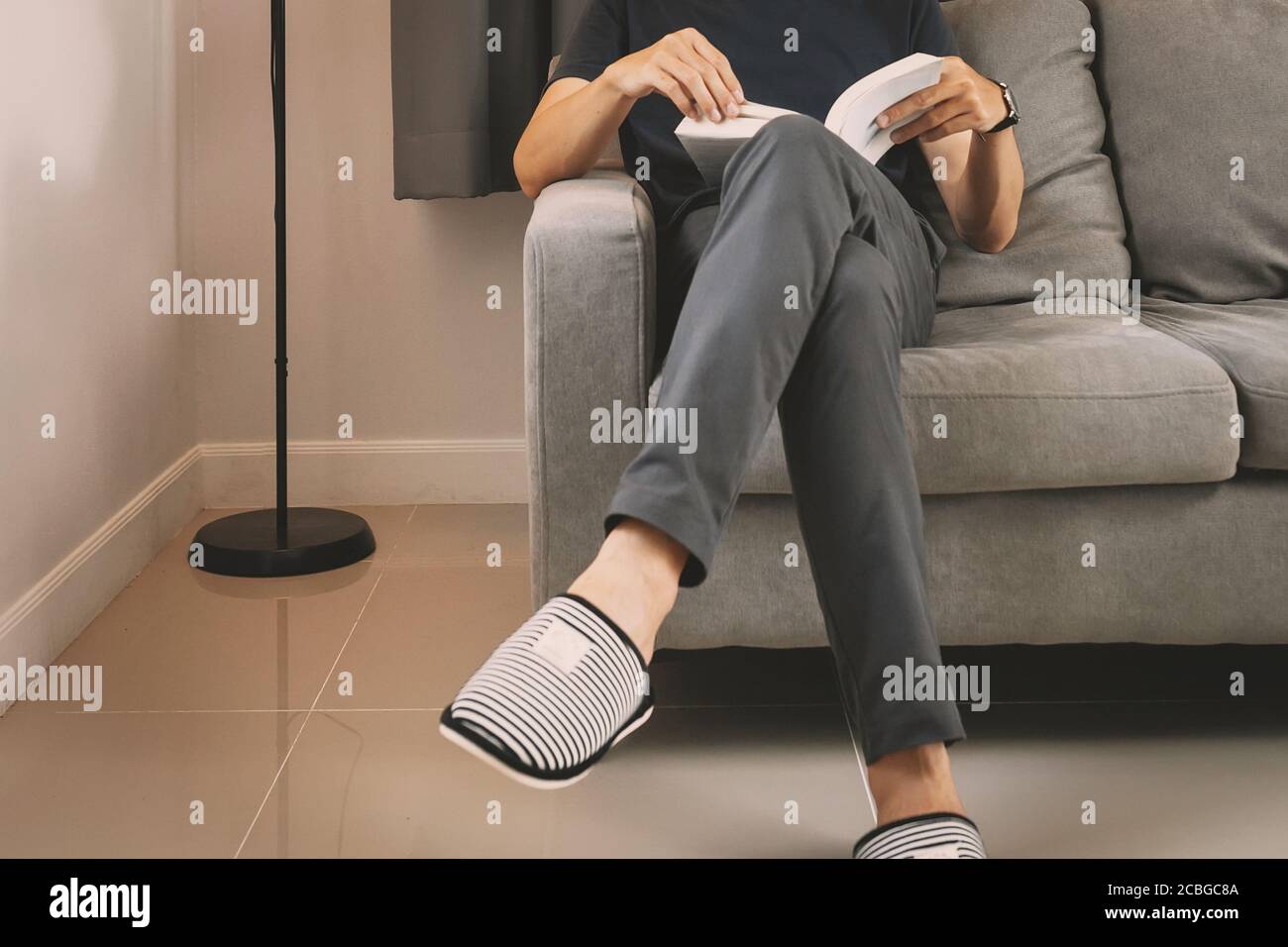 Young man sit down on the sofa reading book at home. Stock Photo