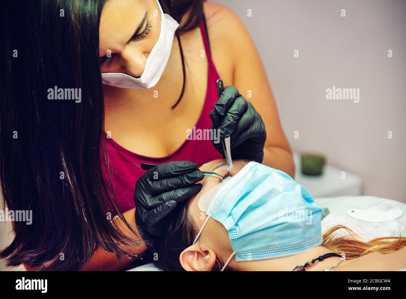woman putting false eyelashes to lady in beauty salon with masks, new normal Stock Photo