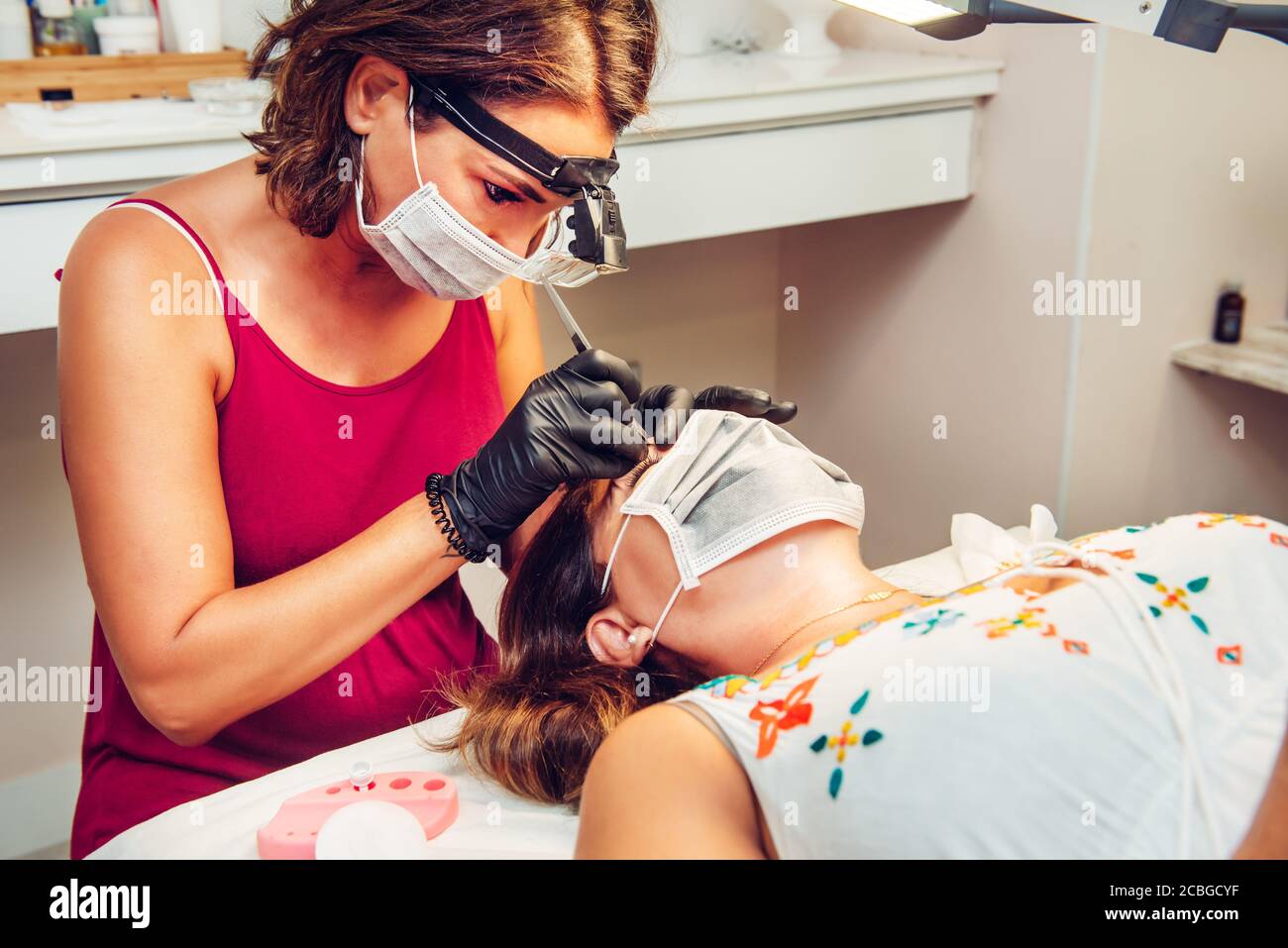 Beautician in beauty center performing an eyebrow treatment to client, with masks during the new normal Stock Photo