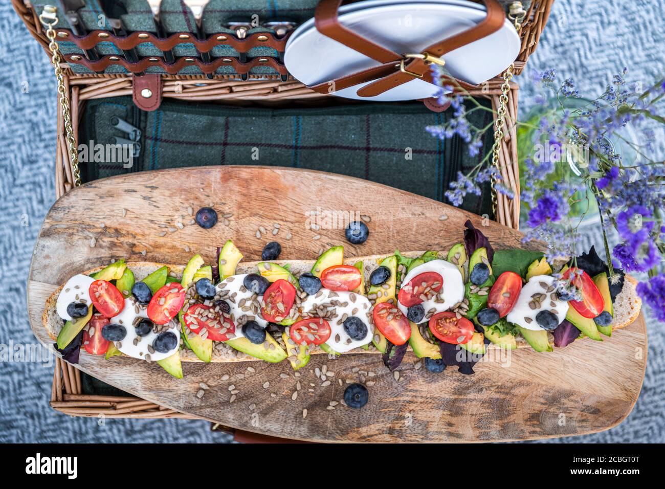 Stylish summer picnic flat lay set up, with a picnic hamper and vegetarian baguette of avocado, tomatoes and mozarella cheese Stock Photo