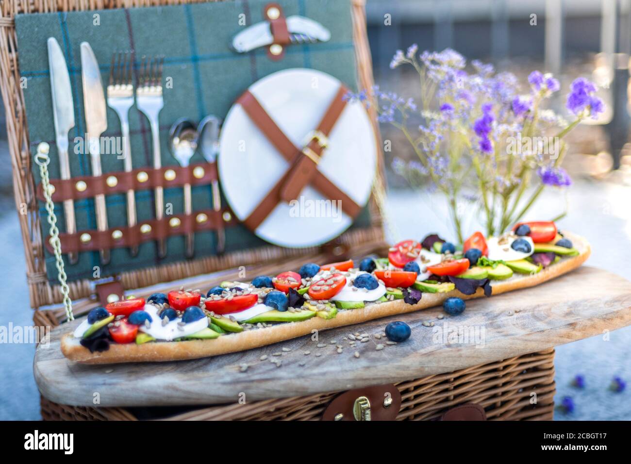 Stylish summer picnic set up, with a picnic hamper and vegetarian baguette of avocado, tomatoes and mozarella cheese Stock Photo