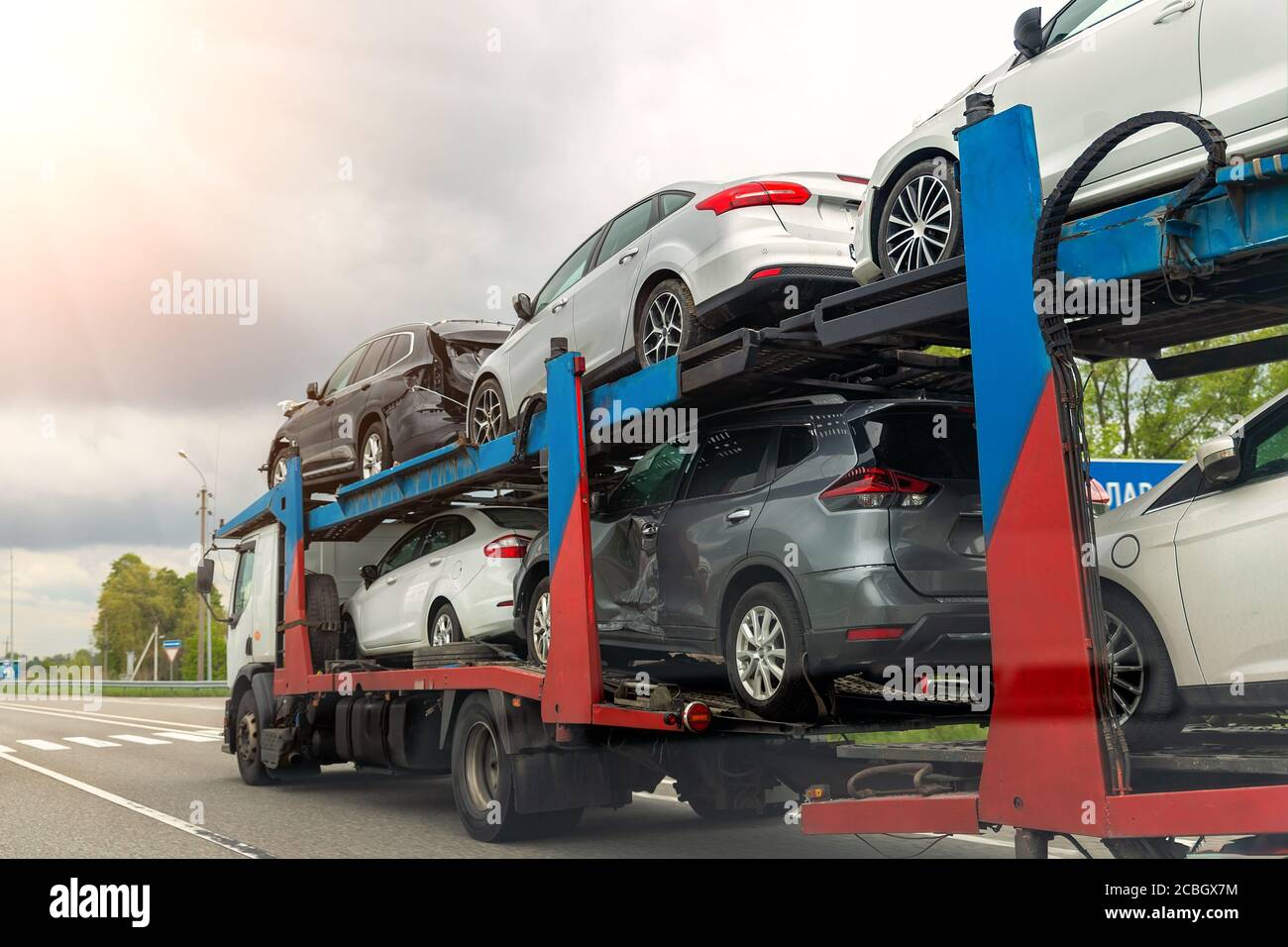 Tow truck car carrier semi trailer on highway carrying batch of damaged cars sold on insurance car auctions for repair and recovery. Vehicles shipment Stock Photo
