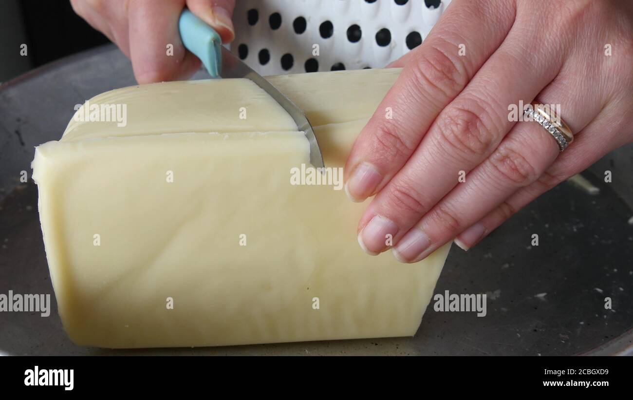 Close-up of female cook or housewife cutting cheese with a knife Stock Photo
