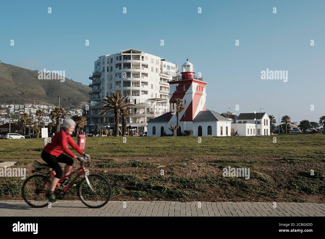 Elderly woman riding her bicycle at the Sea Point Promenade in Cape Town with the Green Point Lighthouse in the background-Motion blur on the cyclist. Stock Photo
