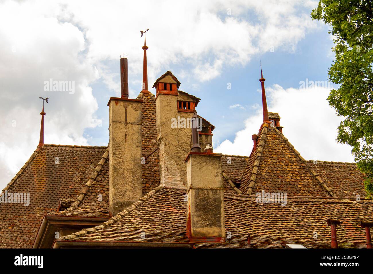 Close up isolated image of a complex traditional roof structure on a historic swiss building. Hexagonal clay tiles cover the steep slope of the roof w Stock Photo