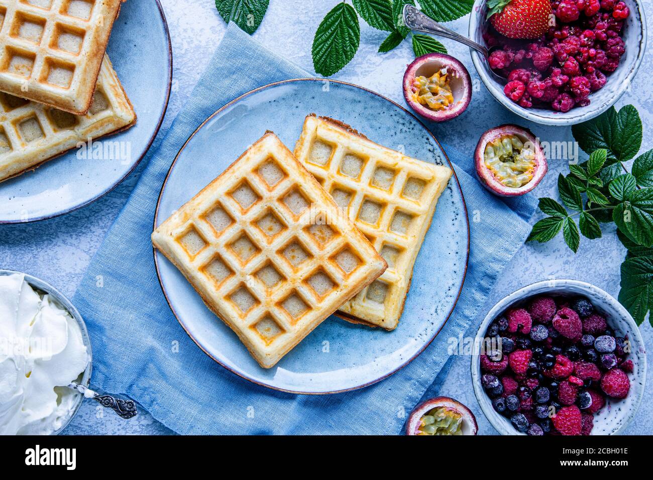 Belgian waffles with raspberries, blueberries and passion fruit. There is a bowl of whipped cream on the table. The food is seen from above, flat lay Stock Photo