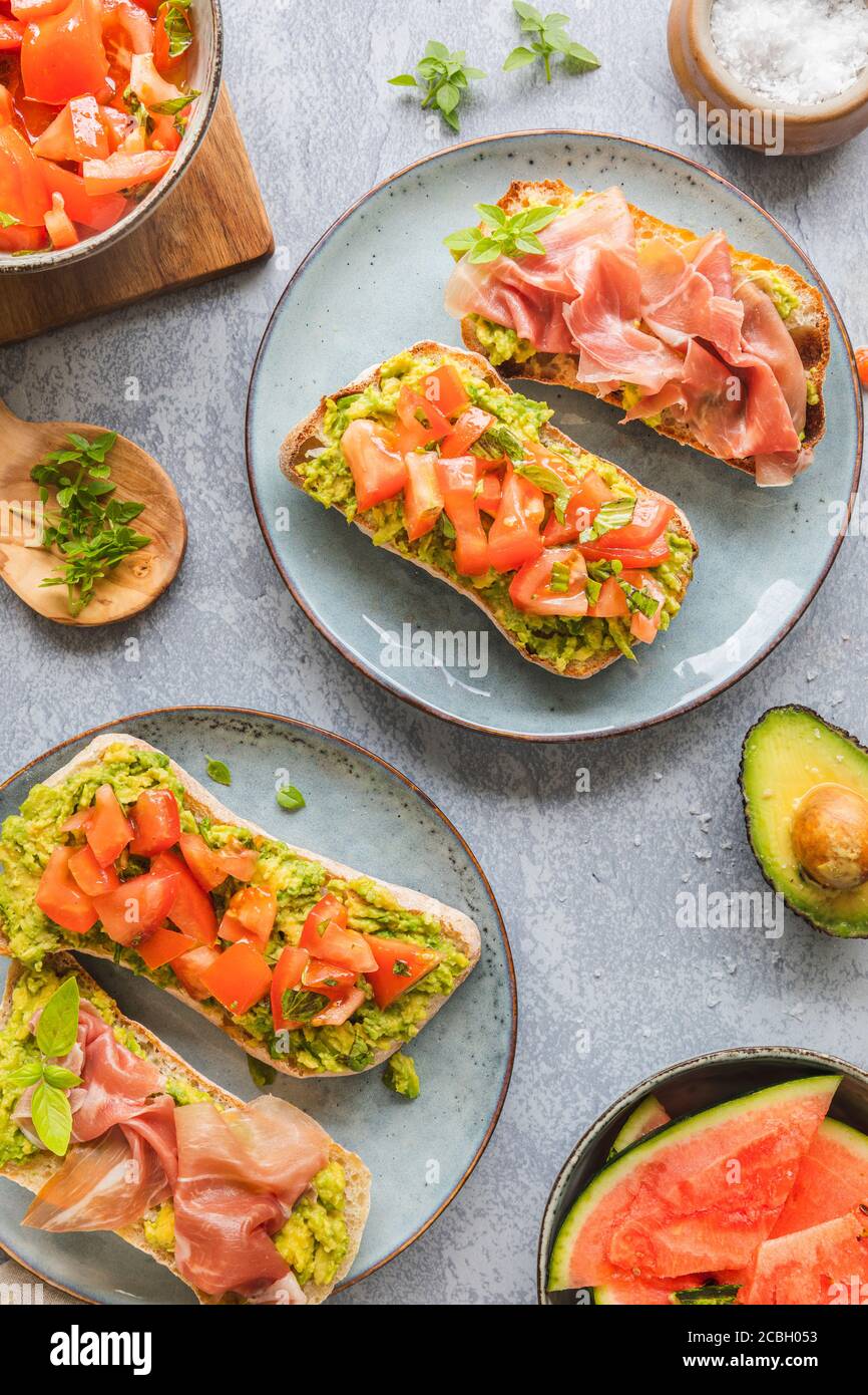 Homemade bread with avocado spread,  chopped tomatoes and herbs. With Parma prosciutto ham. Healthy breakfast concept seen from above. With copy space Stock Photo