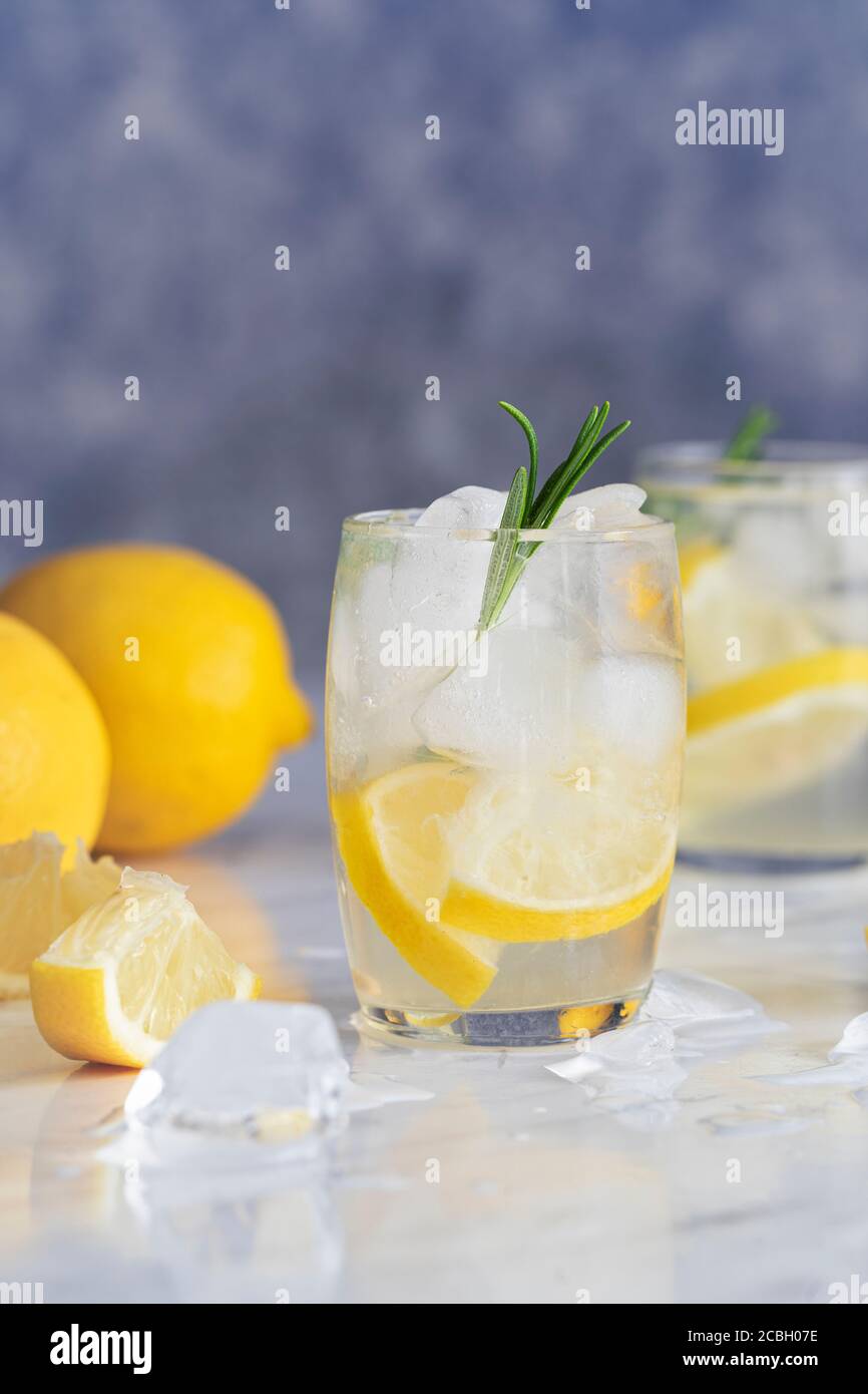 Lemon drink with rosemary and ice. Concept gin and tonic, GT. On a rustic wooden background. Refreshing cocktail or detox mocktail with homegrown herb Stock Photo