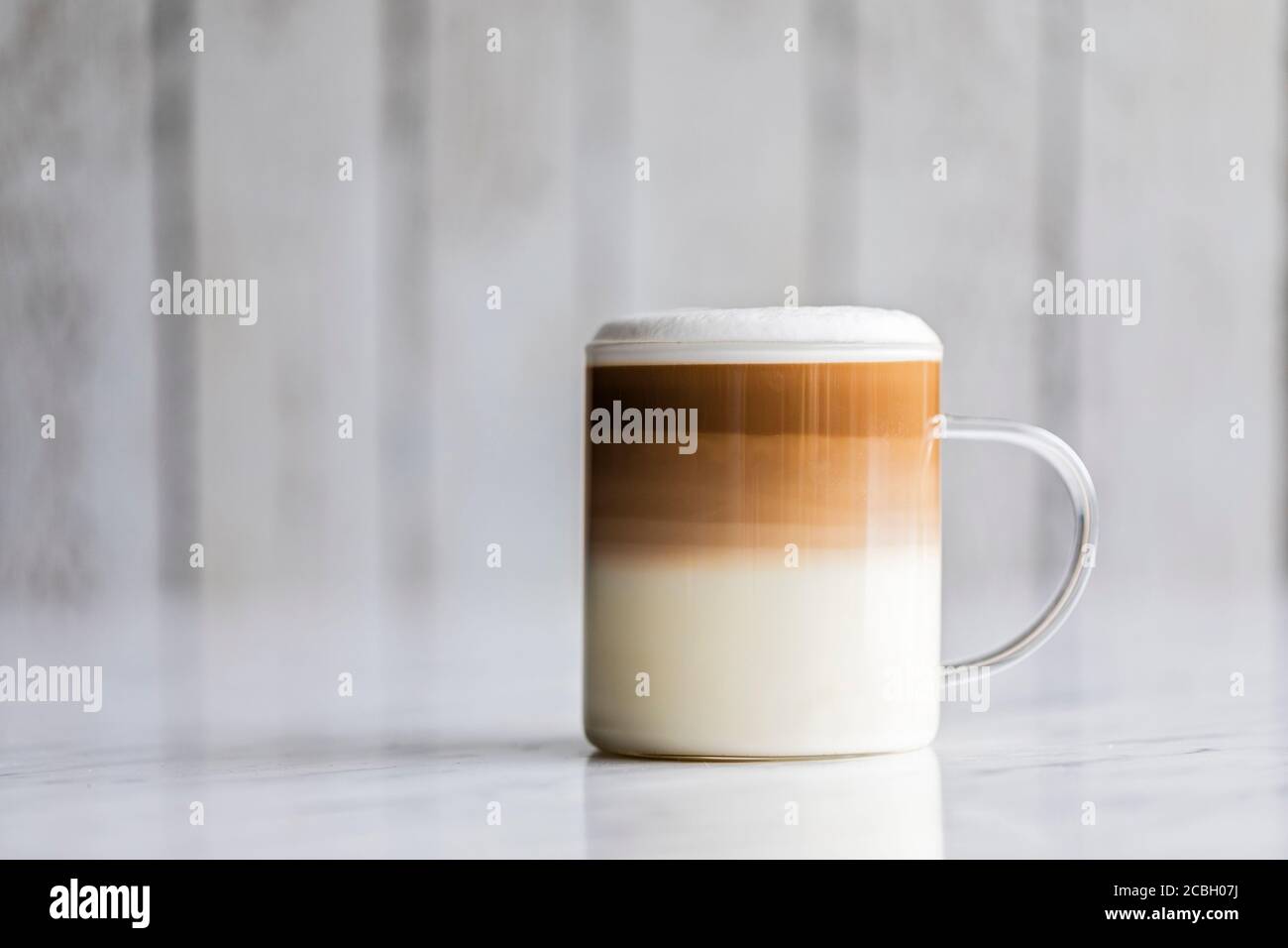 Cafe latte macchiato layered coffee in a see through glass coffee cup. The cup has a white wooden background. Stock Photo