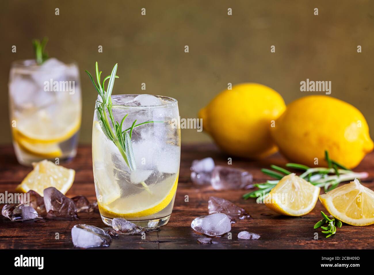 Lemon drink with rosemary and ice. Gin and tonic, GT. On a rustic wooden table. Refreshing cocktail or mocktail detox drink  with homegrown herbs. Cop Stock Photo