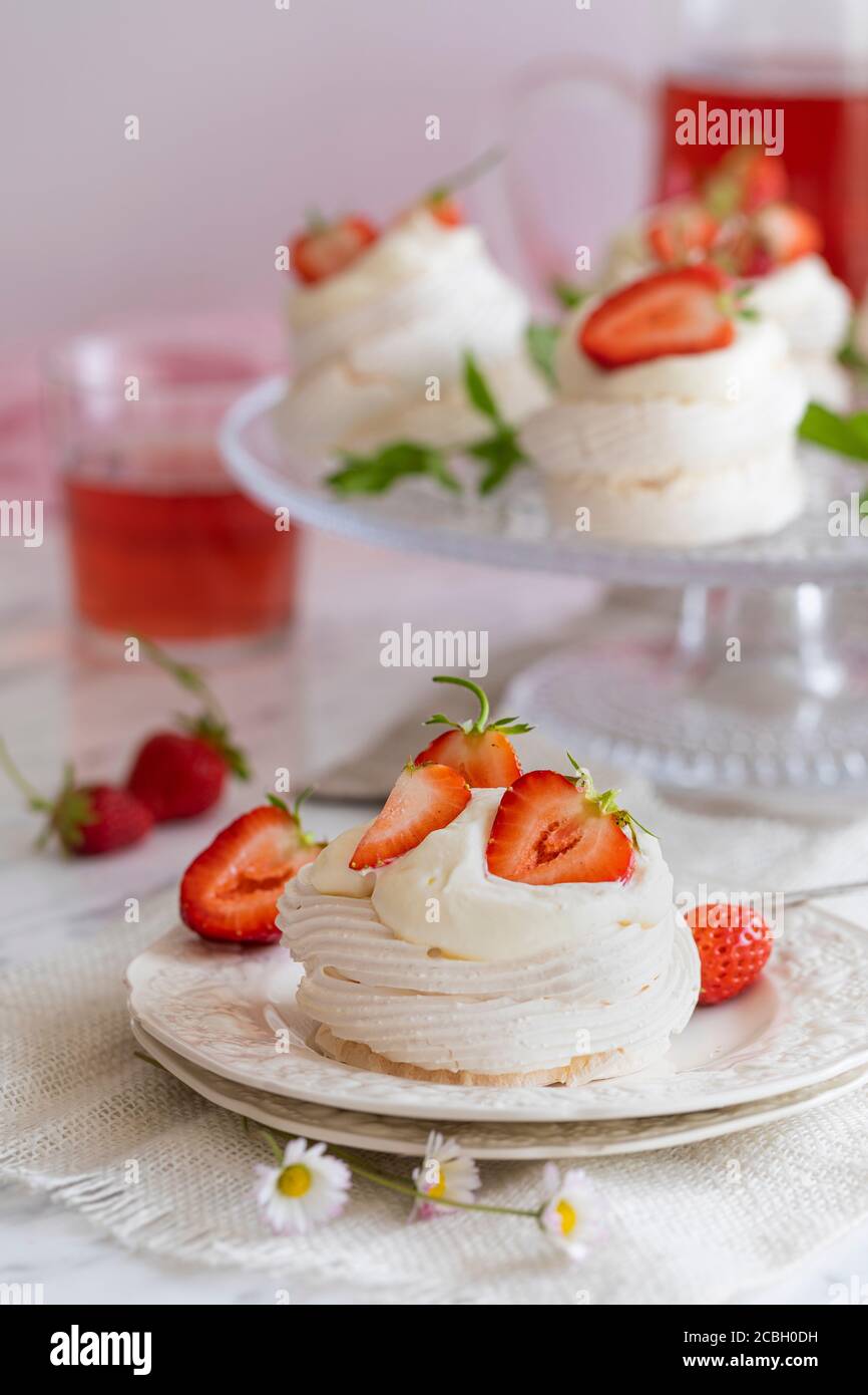 Mini pavlova meringue nests with whipped cream and fresh strawberries. There is some strawberry lemonade on the table and some more pavlova meringues Stock Photo