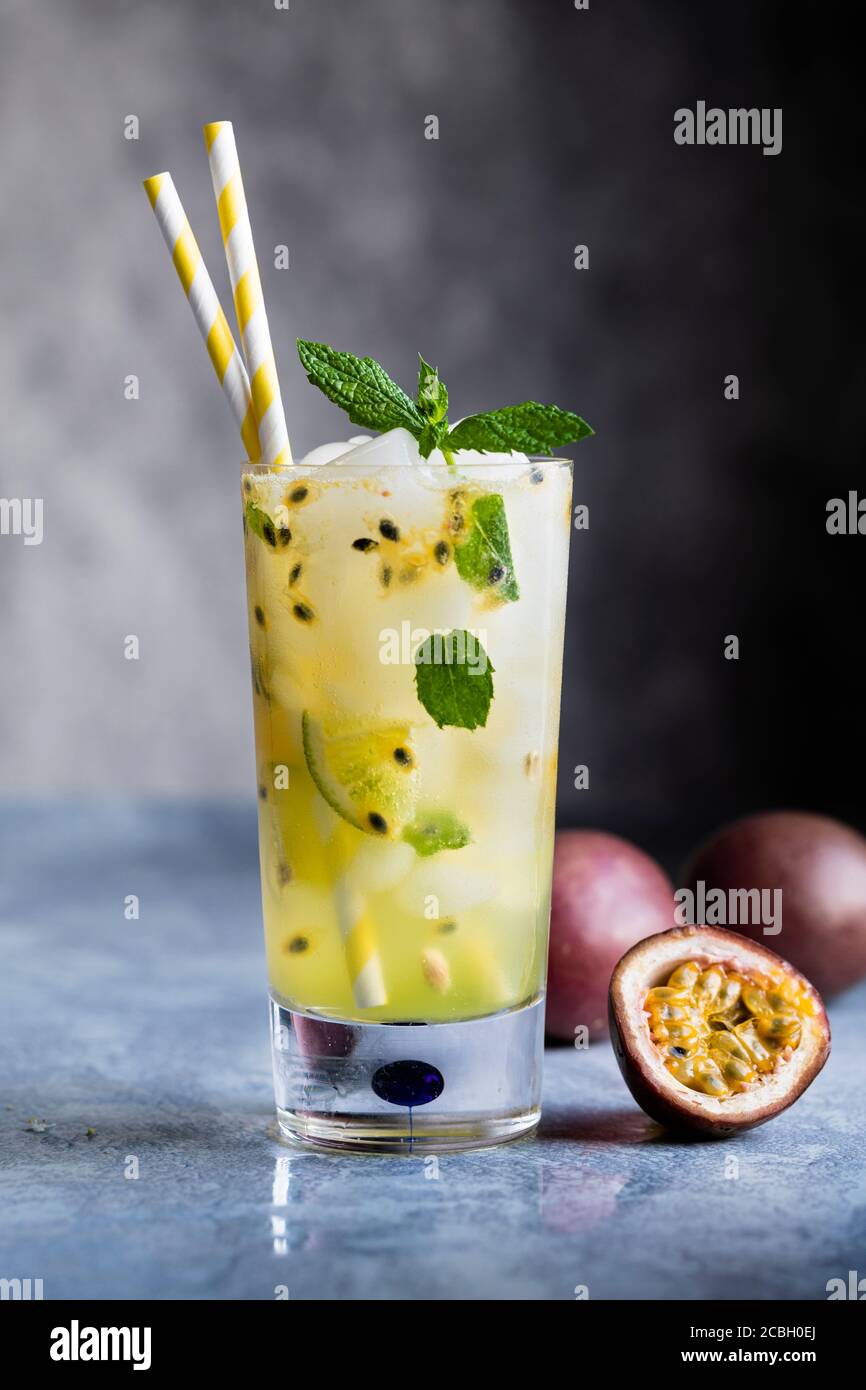 Passion fruit mojito cocktail och mocktail in a high glass, with crushed ice, lime and mint leafs. Passion fruits on the table.  Gray background with Stock Photo