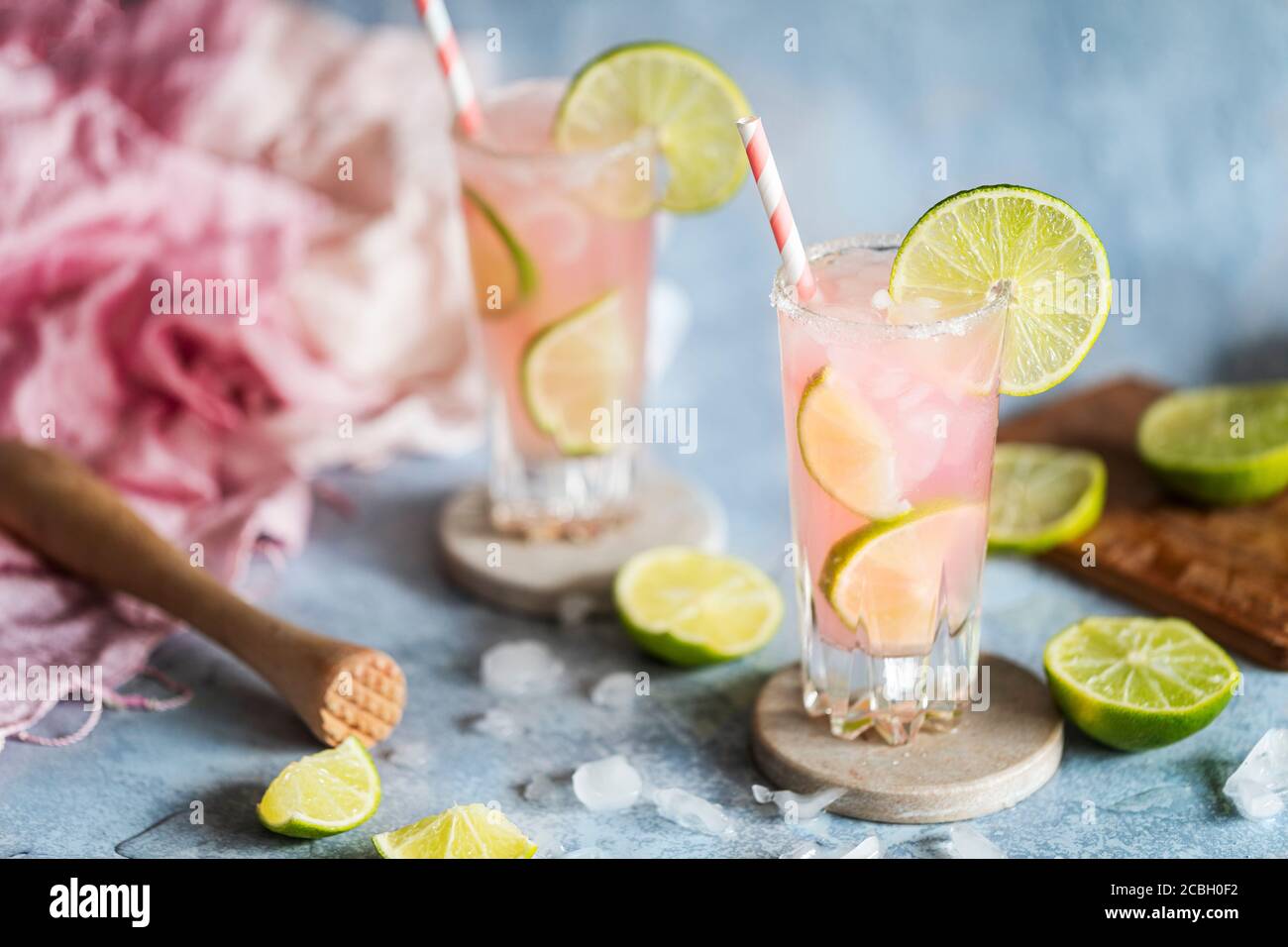 A fresh cocktail drink with lime and pink grapefruit juice. Paloma cocktail. Two glasses on the table and they have environmentally friendly paper str Stock Photo