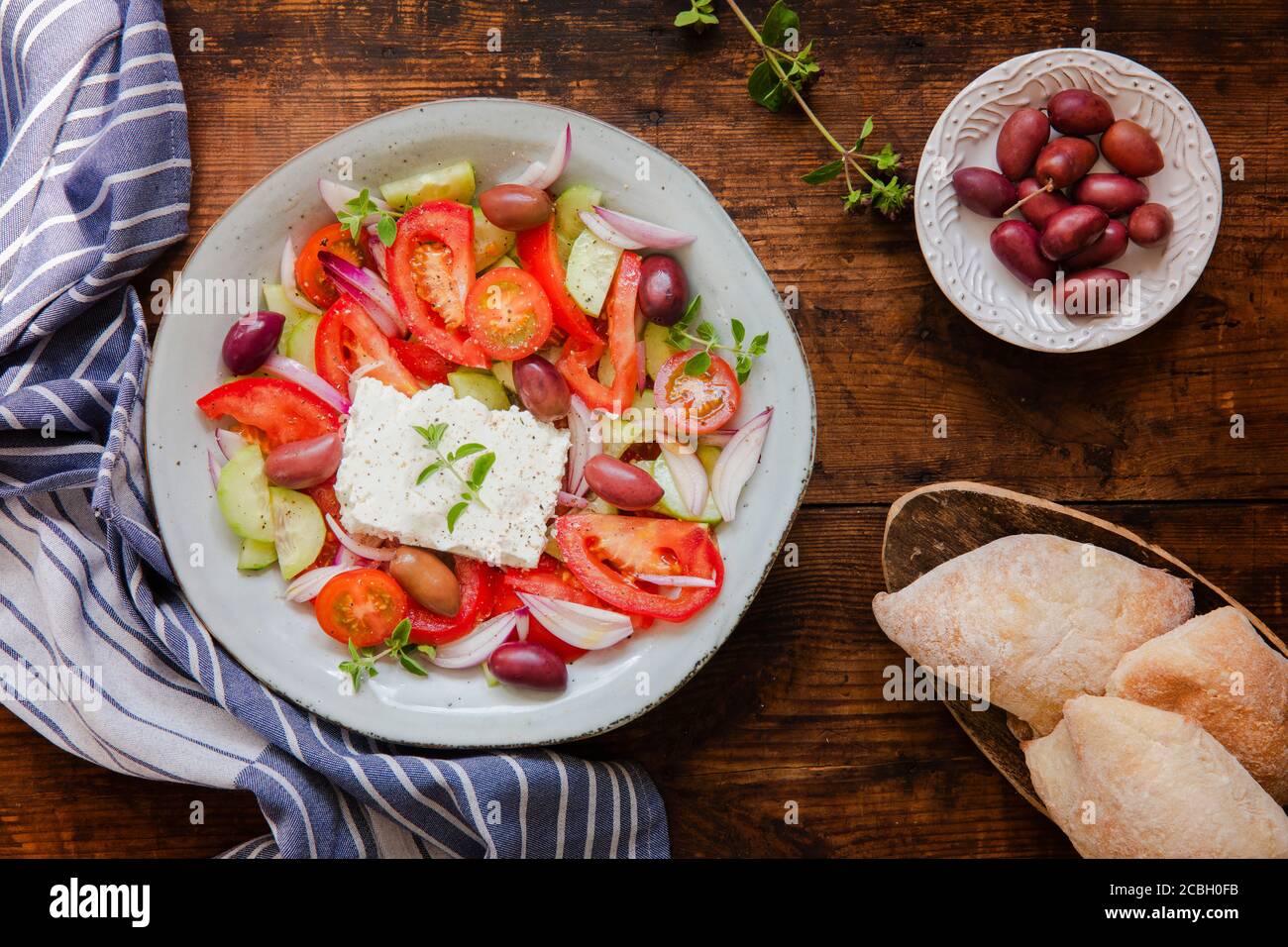 A fresh traditional greek salad horiatiki choriatiki with feta cheese, tomatoes, cucumber, onion and kalamata olives and fresh bread and a blue white Stock Photo