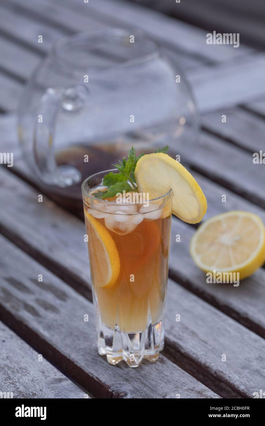 A glass of ice tea with lemon and mint, on a rustic gray aged table with a glass tea pot in the background and half a lemon. Vertical shot with copy s Stock Photo