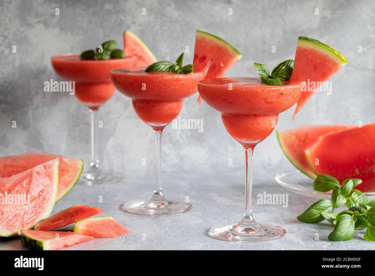 Three  fresh frozen blended margarita drinks with strawberries and watermelon. The drinks are garnished with basil leaves and watermelon. Gray backgro Stock Photo