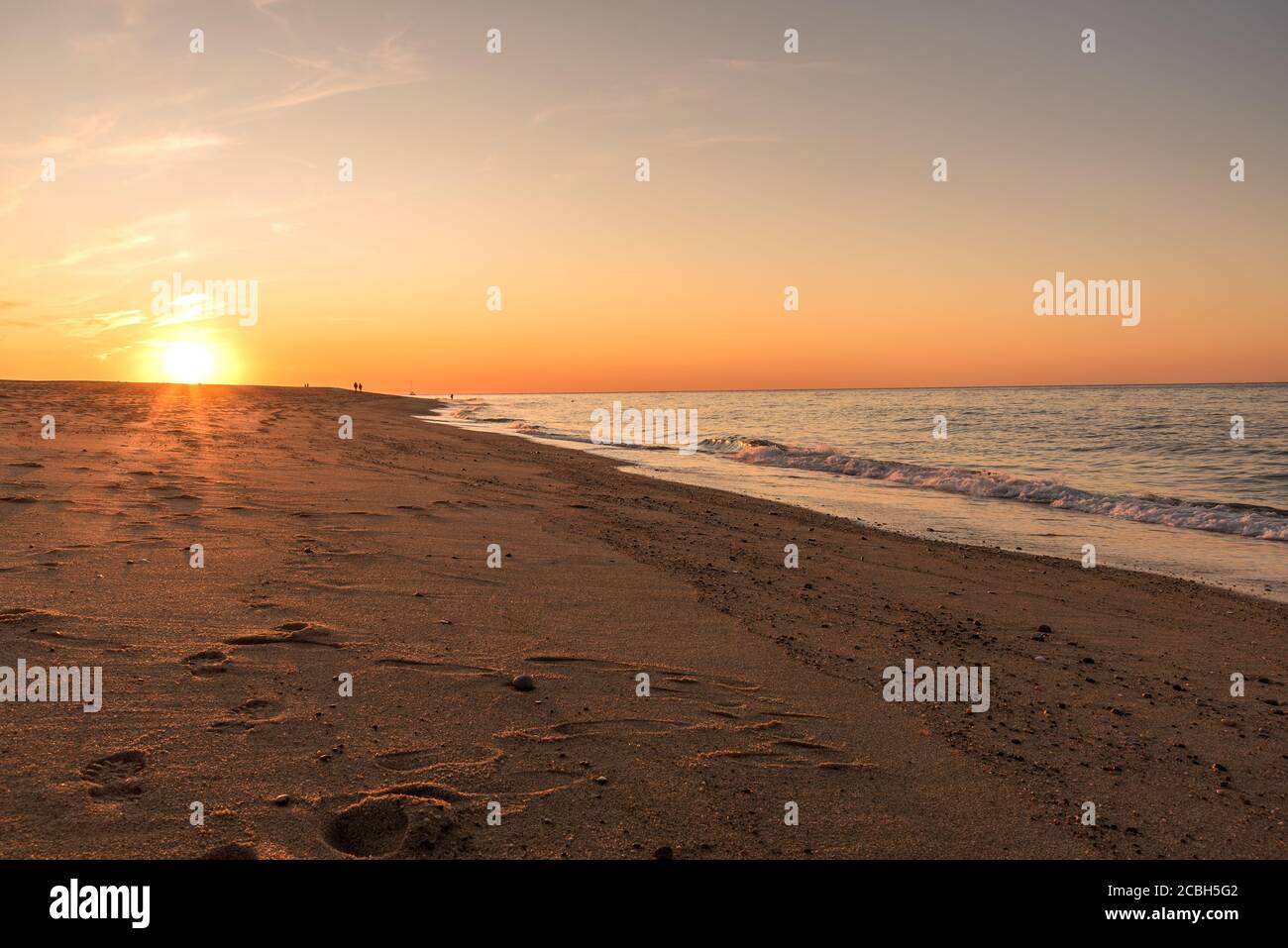 Setting sun over a beautiful sandy beach. People strolling along the beach are visible in distance Stock Photo