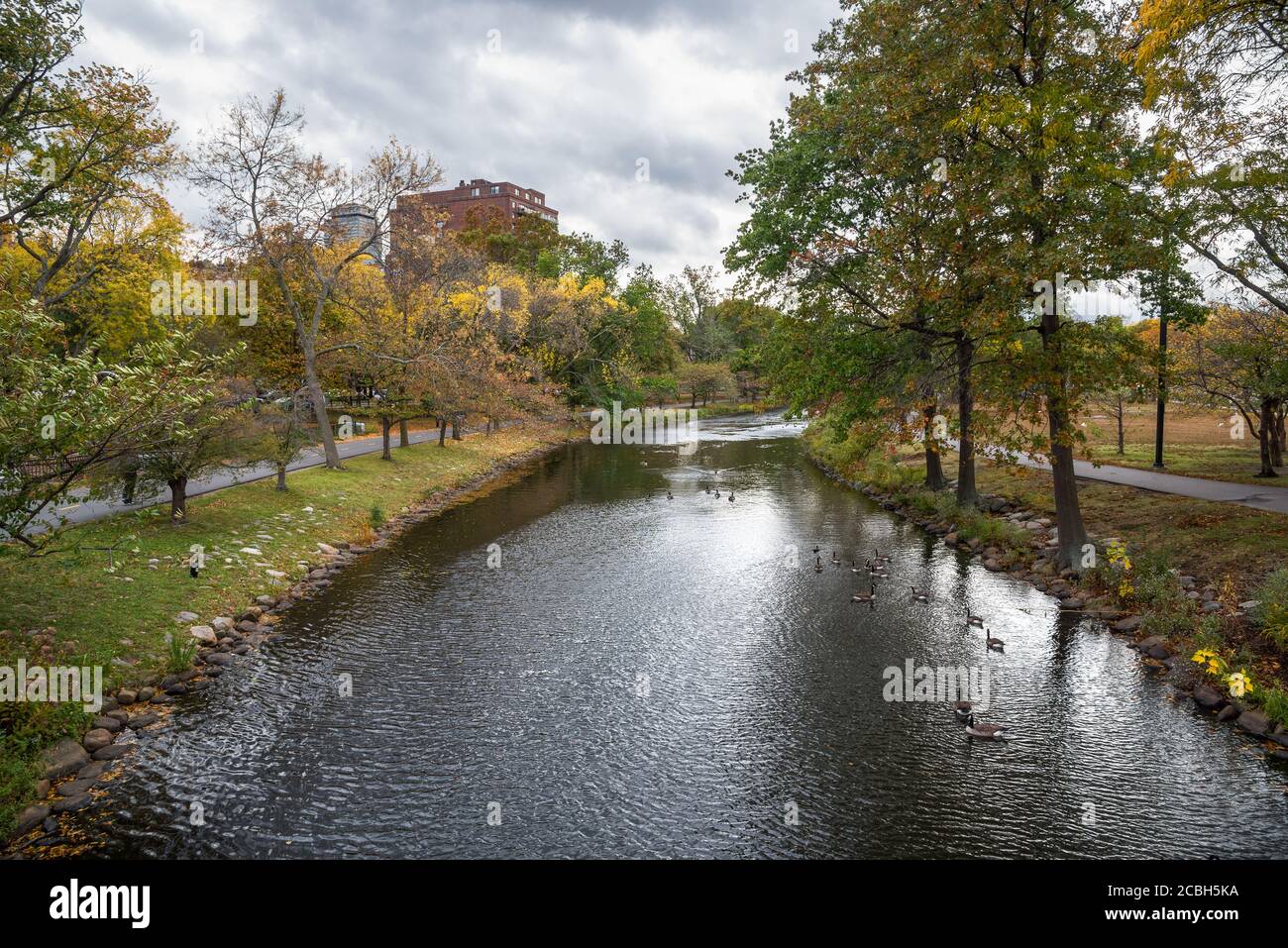 Canal lined with trees and paved paths in a public park under stom clouds on an autumn day Stock Photo