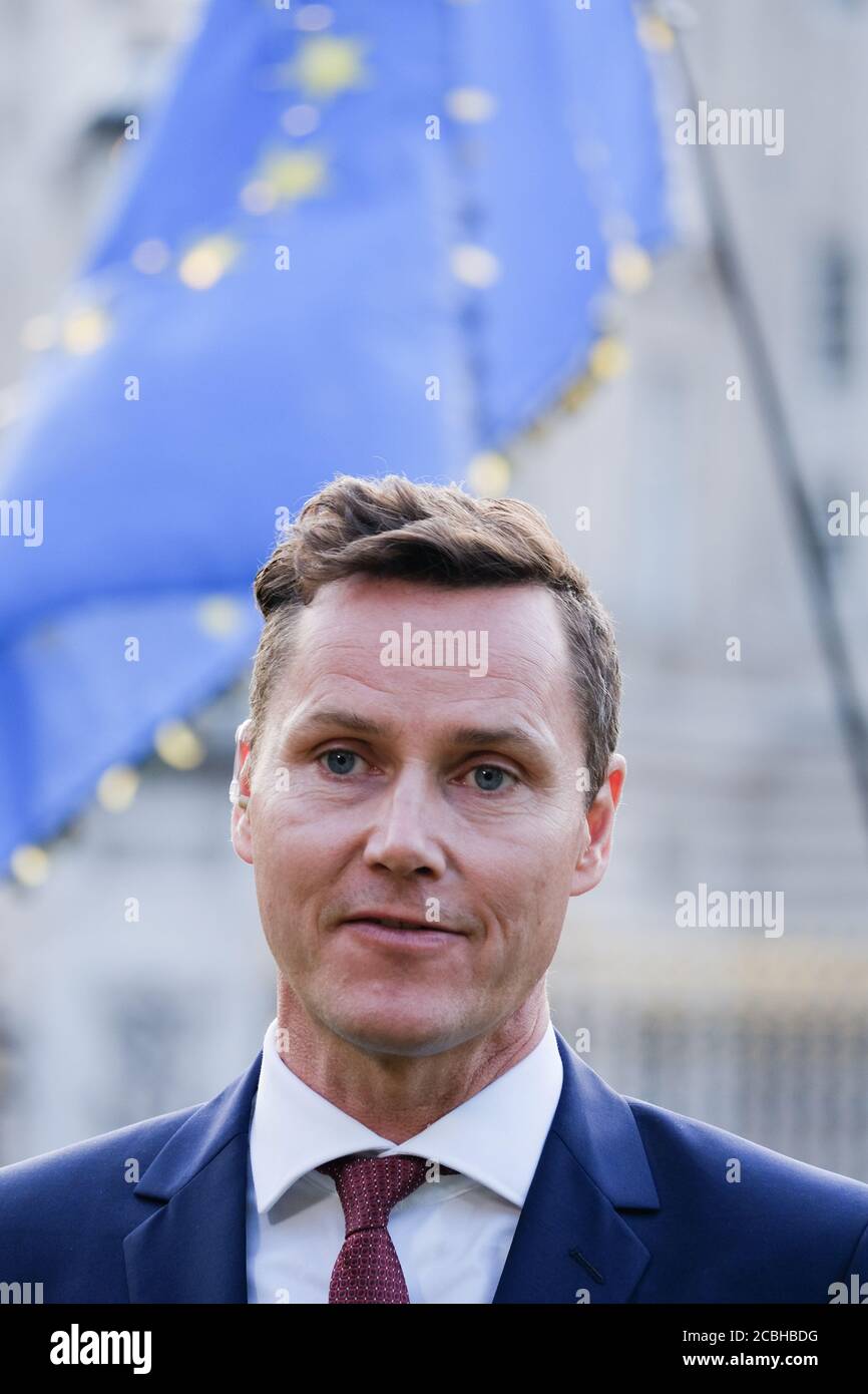A TV news correspondant broadcasts live at an anti-Trump demo during his State visit in 2019.  An EU flag is held by a protester in the background. Stock Photo