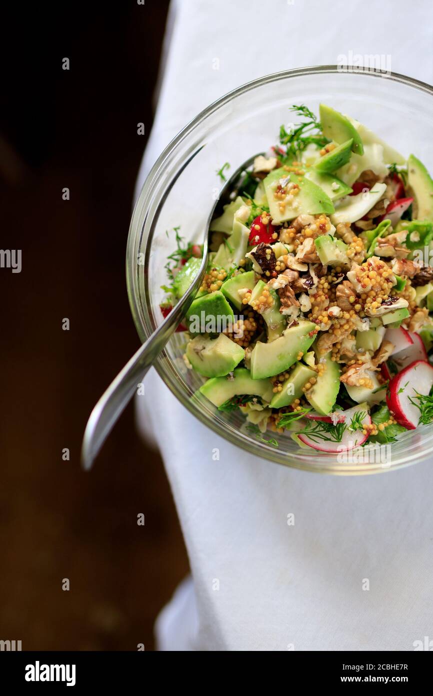 salad in a transparent bowl of avocado, walnuts, green salad, radish French mustard on a table with a white tablecloth. View from above Stock Photo