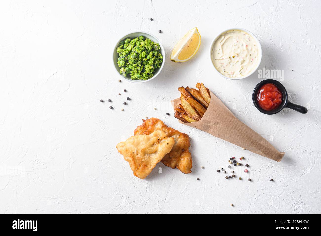 Fried fish and chips in a paper cone on white background with all