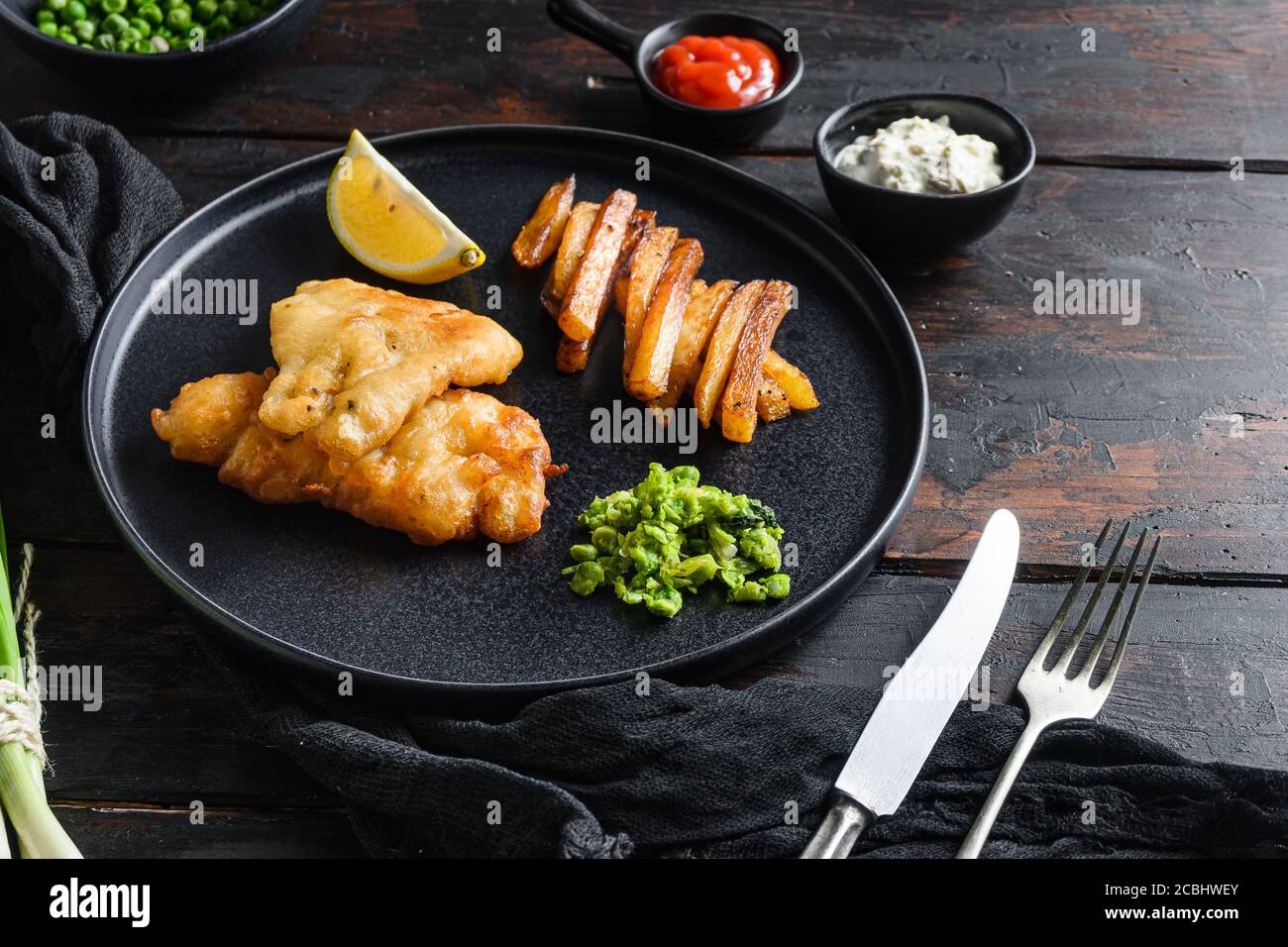 Fish & chips with dip and lemon black plate with British traditional cusine food with beer-battered cod and fries and a side of tartar sauce mushy Stock Photo