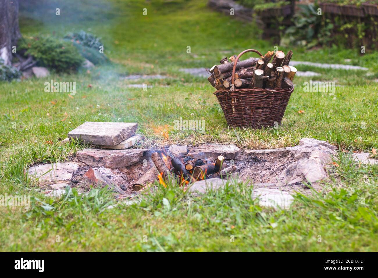 camp fire in the garden, next to a basket with firewood Stock Photo