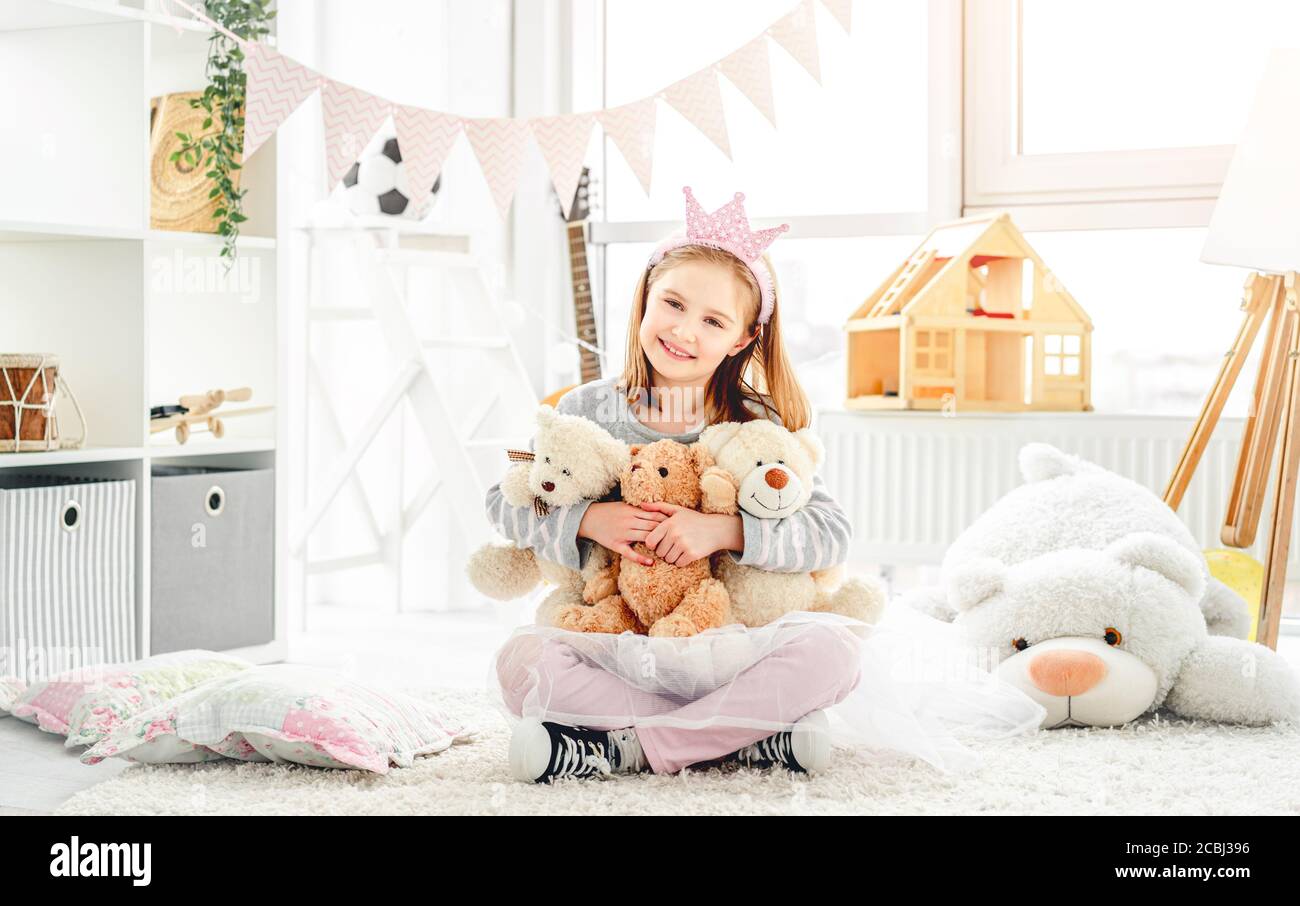 Smiling little girl hugging teddy bears sitting on floor indoors Stock ...