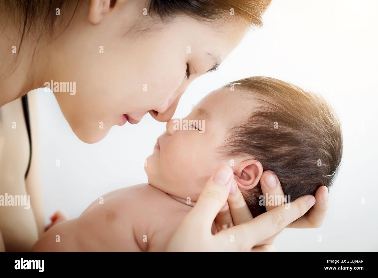 Concept of love and family relationship : Portrait of happy Asian mother use nose touch newborn cute little baby nose on a white bed at home. Stock Photo