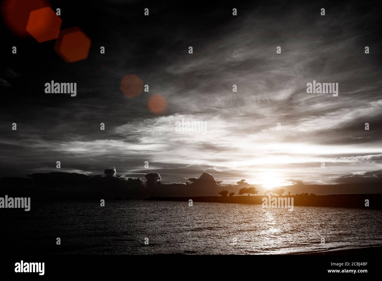 sunset on cloudy sky at the sea beach with silhouette rock bridge and tree background , black and white color with red lens flare effect Stock Photo