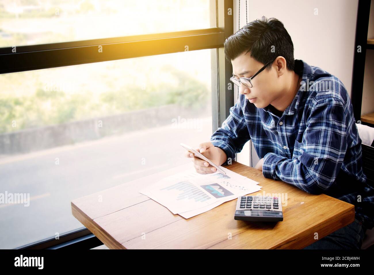 Business accounting people, saving, finance , economy concept. Serious Asian businessman using smartphone with calculator , paperwork for statistic Stock Photo
