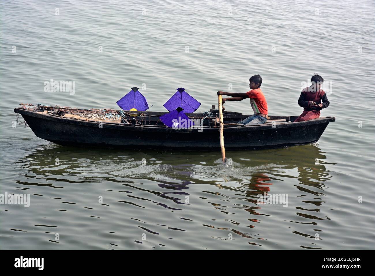 In Varanasi, two boys are collecting kites from the river Ganges and leaving it in a boat. Lots of kites are flown in Varanasi in winter. Stock Photo