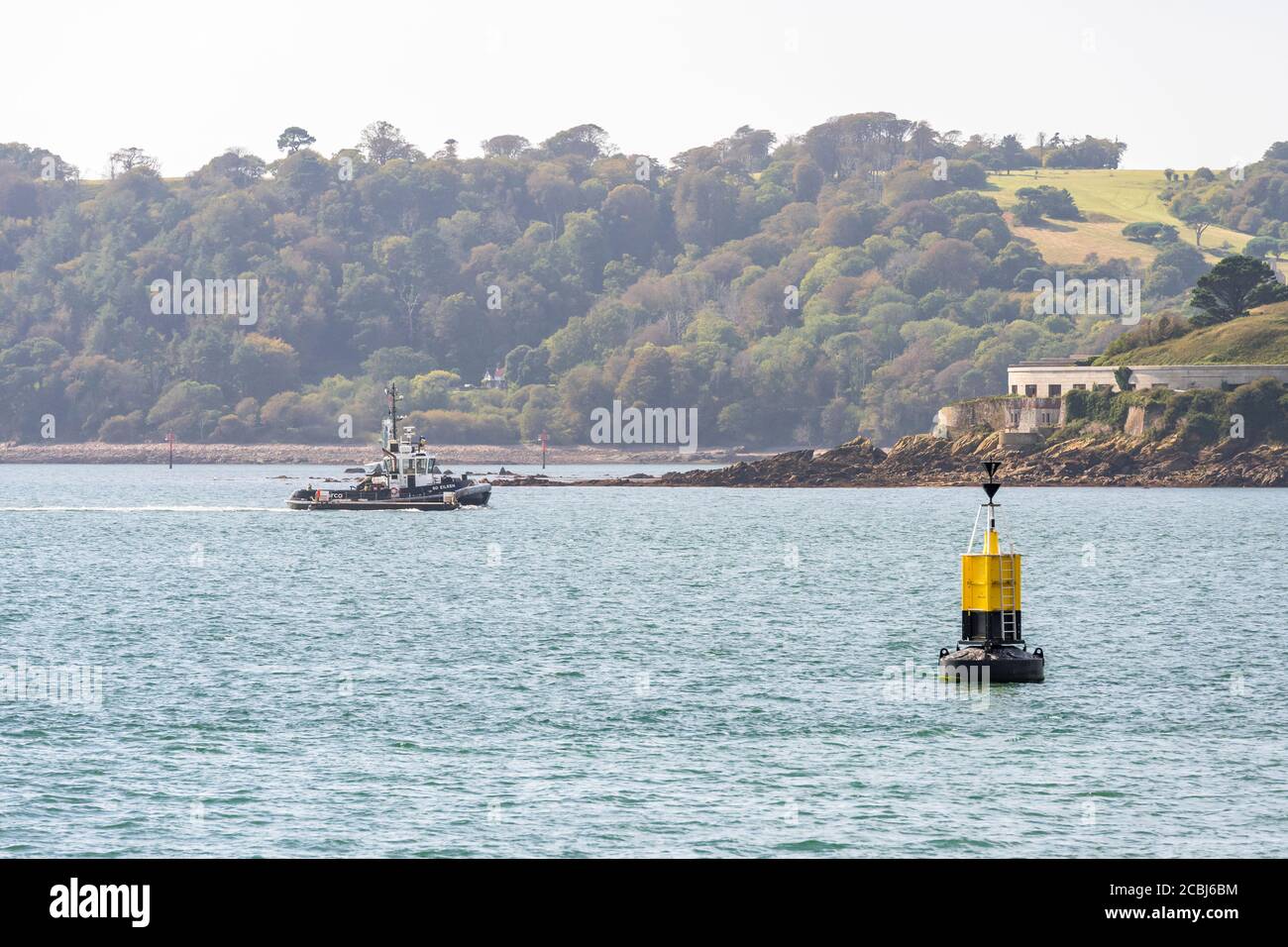 Serco ASD Tug boat SD Eileen returning from at anchor HMS Argyll through Plymouth Sound passing Drakes Island a pontoon hitched to her starboard beam Stock Photo