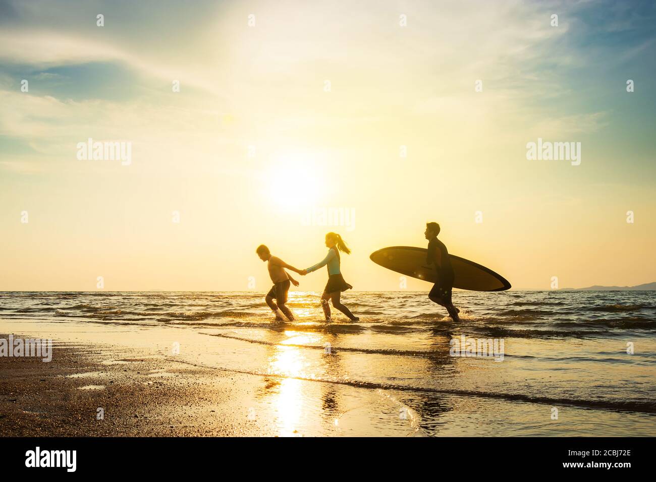 Outdoor sport activity friendship concept : Silhouette of group of young joyful surfer friend running into the sea with surf boards on sunset beach Stock Photo