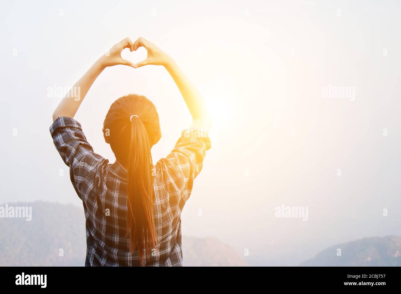 I love travel concept : Freedom traveler woman standing with heart shaped hands and enjoy a wonderful nature at sunrise with morning light effect Stock Photo