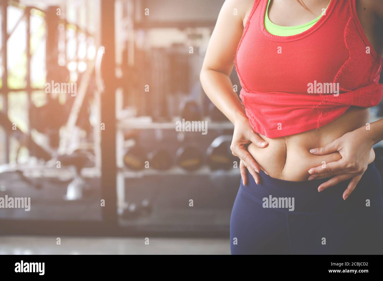 Fat woman, Obese woman hand holding excessive belly fat isolated on gym background, Overweight fatty belly of woman, Woman diet lifestyle concept to r Stock Photo