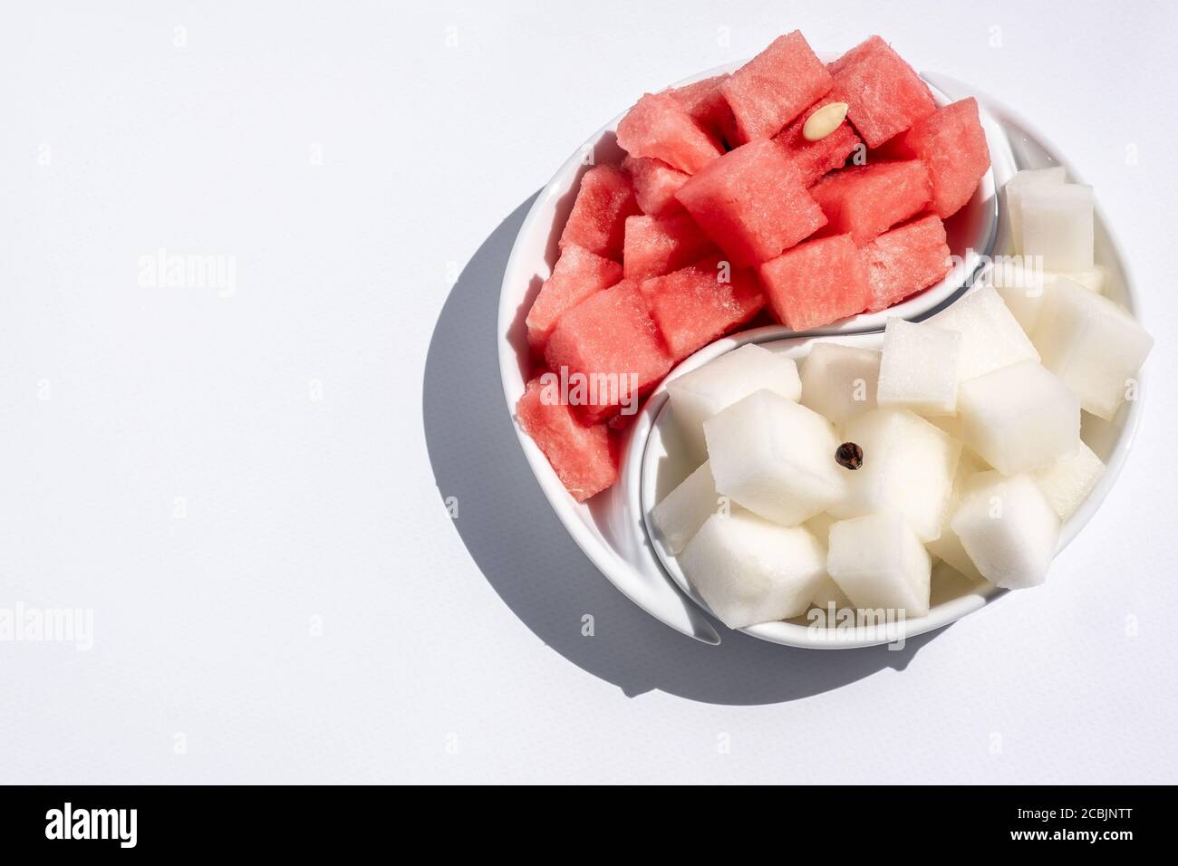 Ripe watermelon and melon, cut into cubes, laid out on a yin-yang dish. Juicy, ripe summer fruits. Bright light. Space for text. Stock Photo